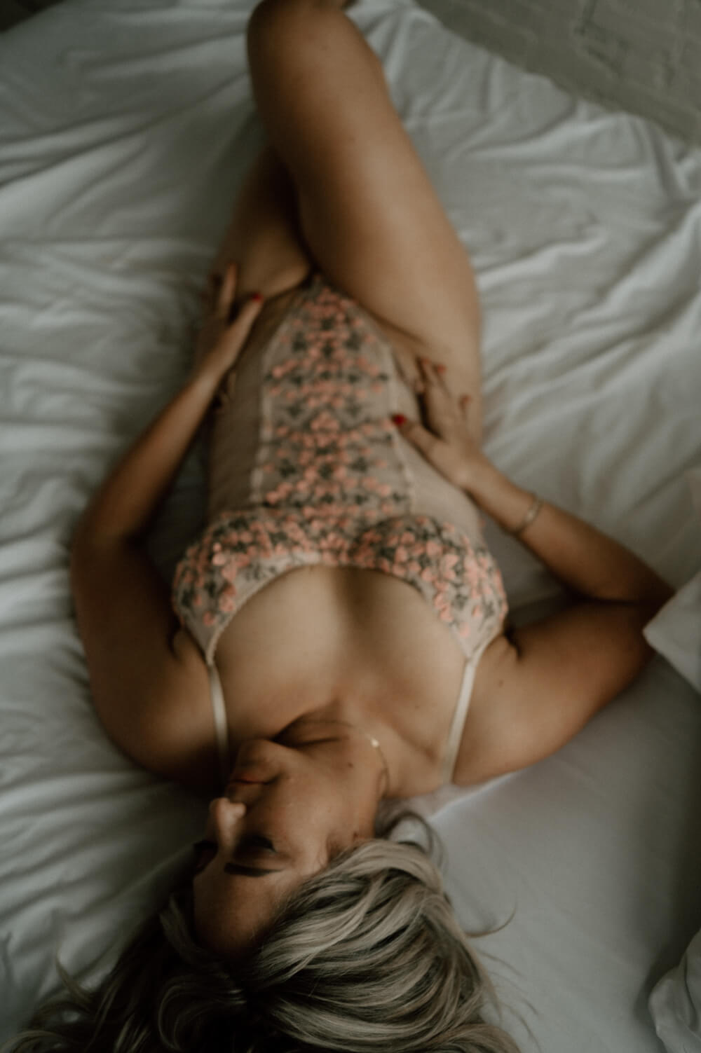 Woman lying on a bed on her back with one knee up, wearing a floral and tan bodysuit excited about seattle date night ideas