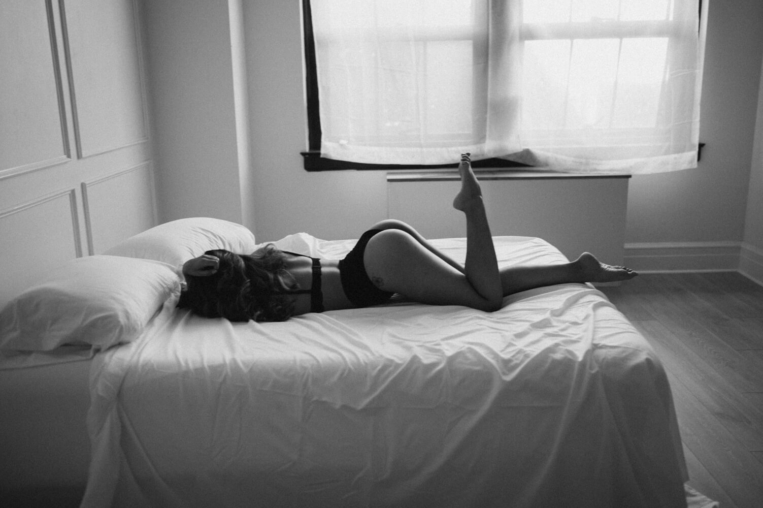 Woman laying on a white bed wearing black underwear set with one leg up