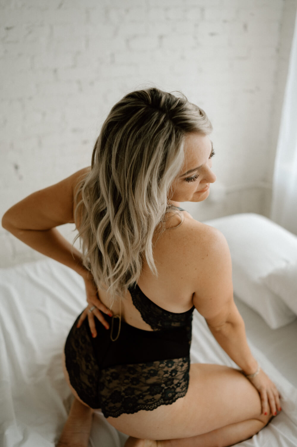 Crossed back black lace bodysuit on tanned woman on a bed